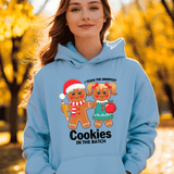 Person wearing a light blue hoodie with a gingerbread design and text, standing outdoors with trees in the background.
