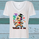 White V-neck t-shirt with a colorful graphic of a teddy bear holding a heart and a bottle, with text 'Thinking of You' on a wooden background.