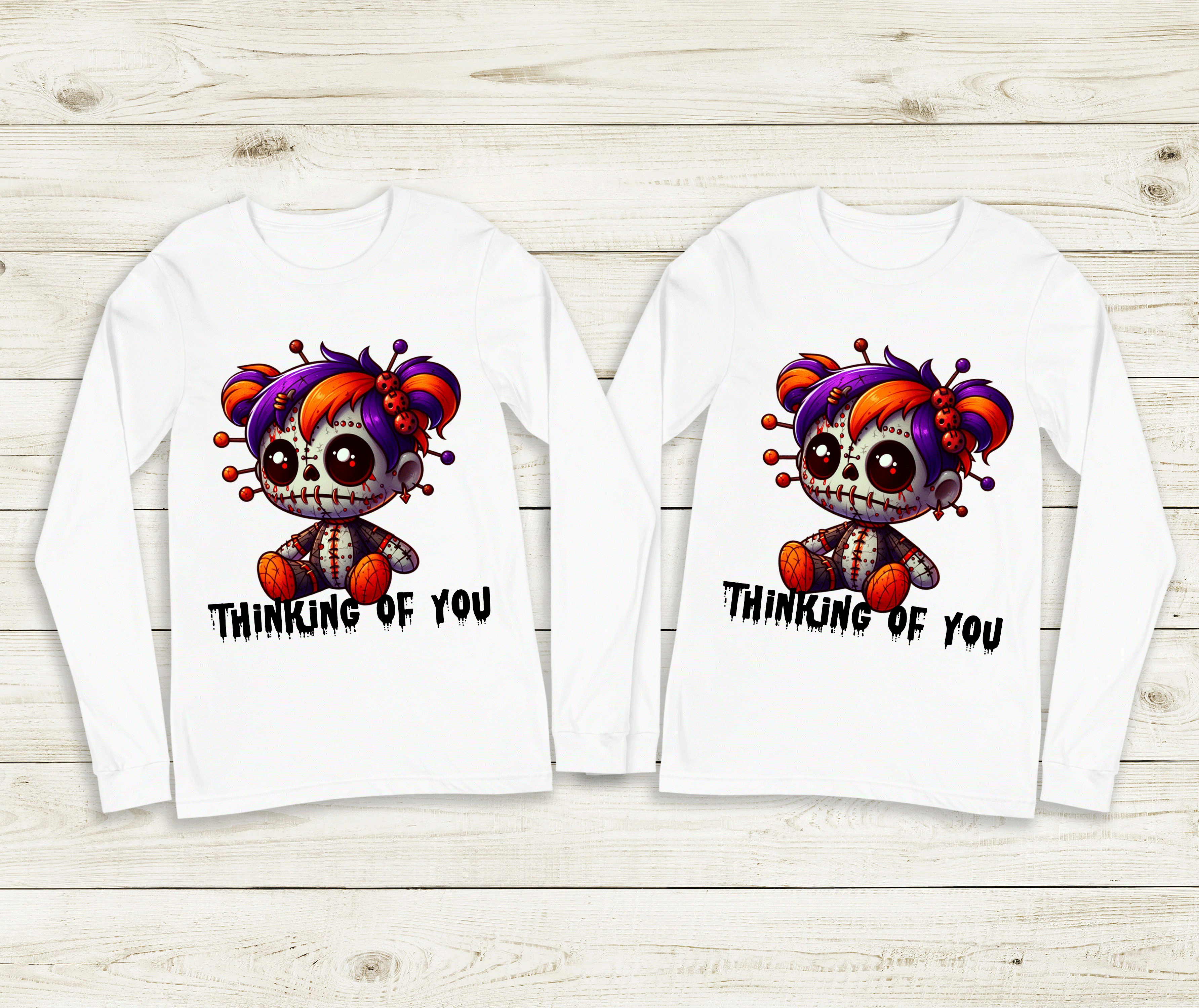 Two white long-sleeve shirts with a cartoon character and 'Thinking of You' text on a wooden surface.