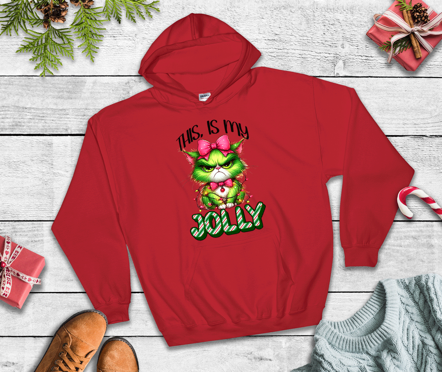 Red hoodie with Grinch design and 'This is my jolly' text on a wooden surface with Christmas decorations.
