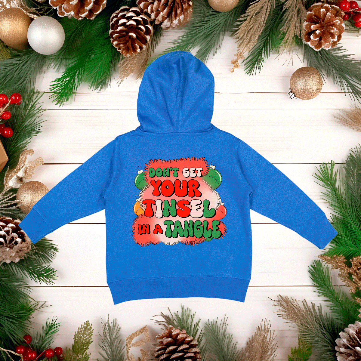 Blue hoodie with festive text on a wooden background with Christmas decorations