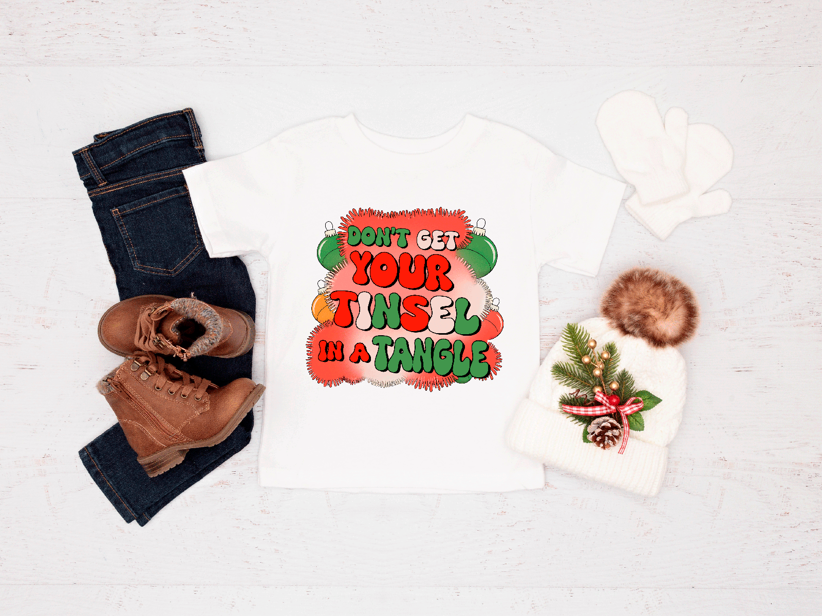 Holiday-themed items including a tee, jeans, boots, and a hat with tinsel text on a white background