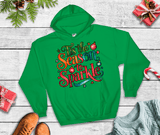 Green hoodie with 'It's the Season to Sparkle' text on a wooden surface with Christmas decorations.