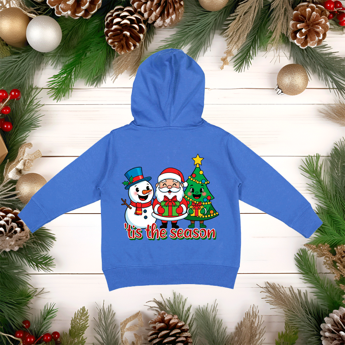 Blue hoodie with Christmas-themed design on a wooden surface with holiday decorations.