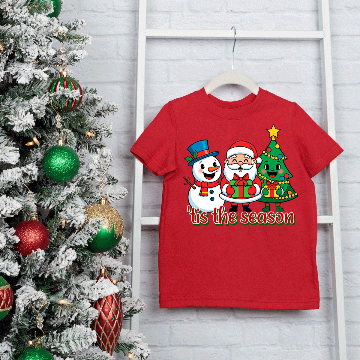 Red t-shirt with Santa Claus and snowman design next to a decorated Christmas tree.