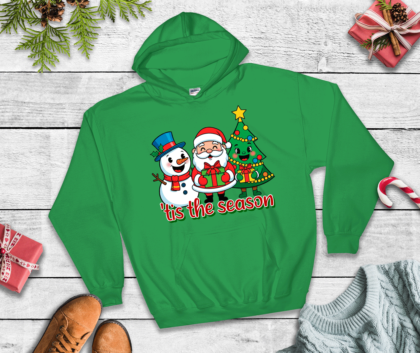 Green hoodie with Christmas design featuring Santa Claus and a snowman on a wooden surface.