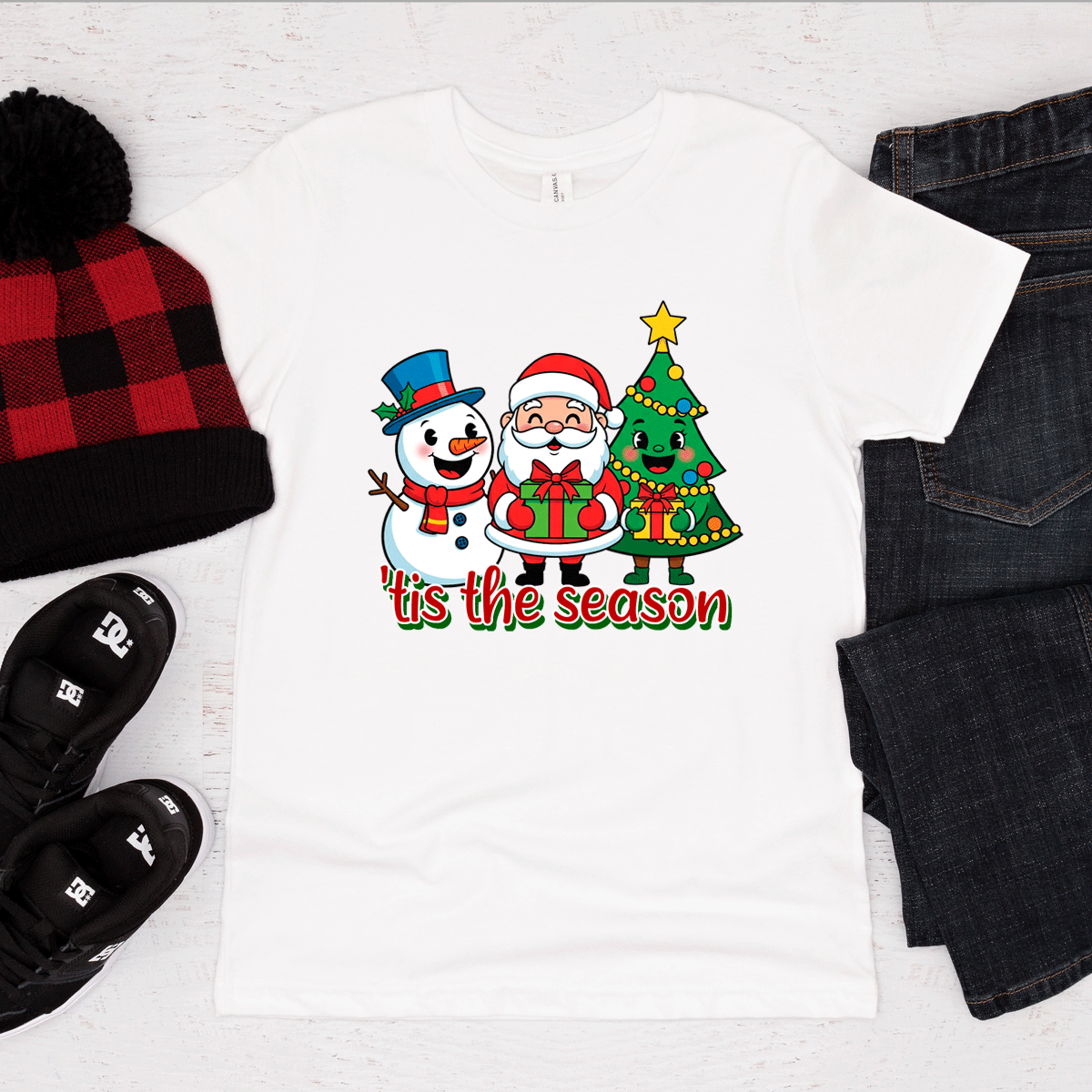 White t-shirt with Christmas design featuring Santa, snowman, and tree, surrounded by festive items on a white background.