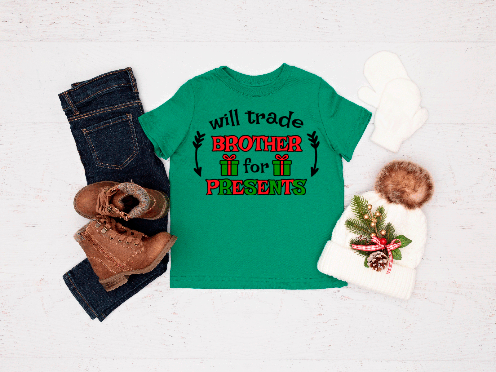 Green t-shirt with Christmas-themed text, jeans, boots, and a decorative bag on a light background