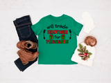 Green t-shirt with Christmas-themed text, jeans, boots, and a decorative bag on a light background