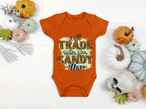 Orange baby onesie with Halloween text on a white surface with pumpkins and decorations.