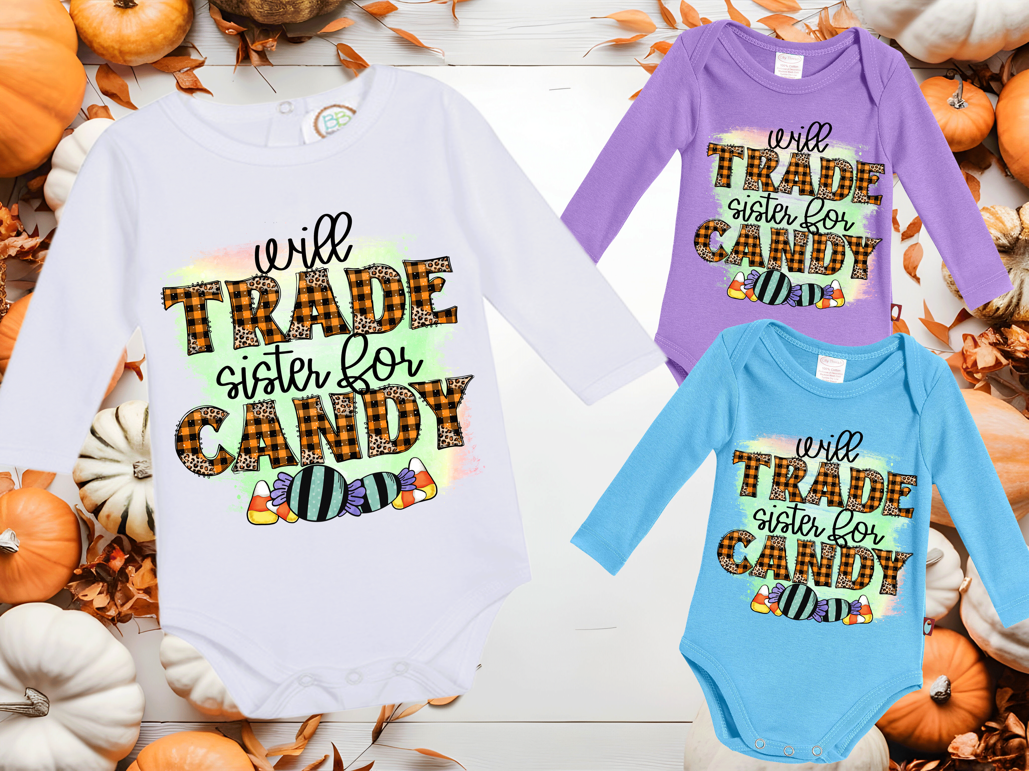 Three Halloween-themed baby onesies with colorful text on a wooden surface with pumpkins and leaves.