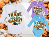Three Halloween-themed baby onesies with colorful text on a wooden surface with pumpkins and leaves.