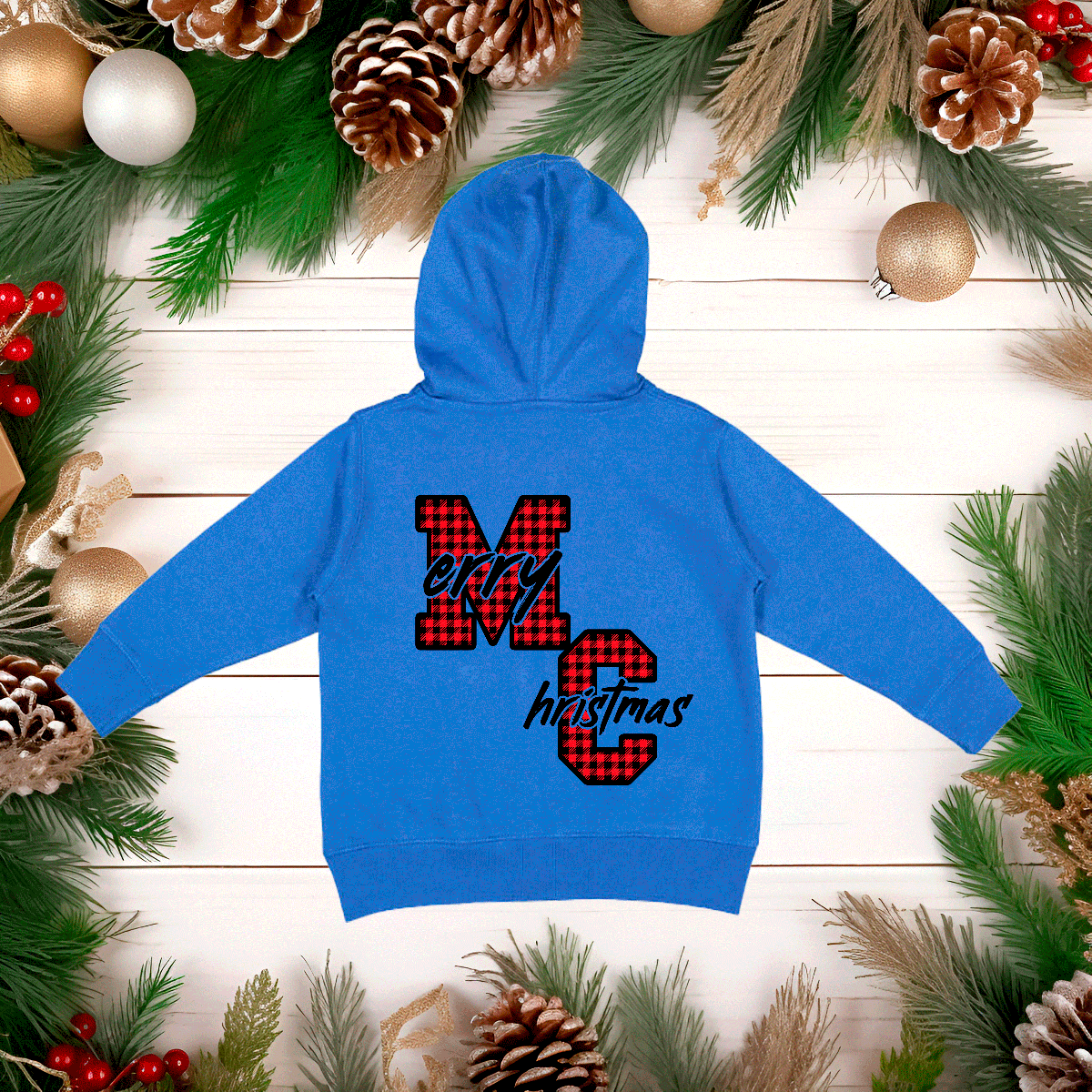 Blue hoodie with 'Merry Christmas' design on a wooden surface with holiday decorations.
