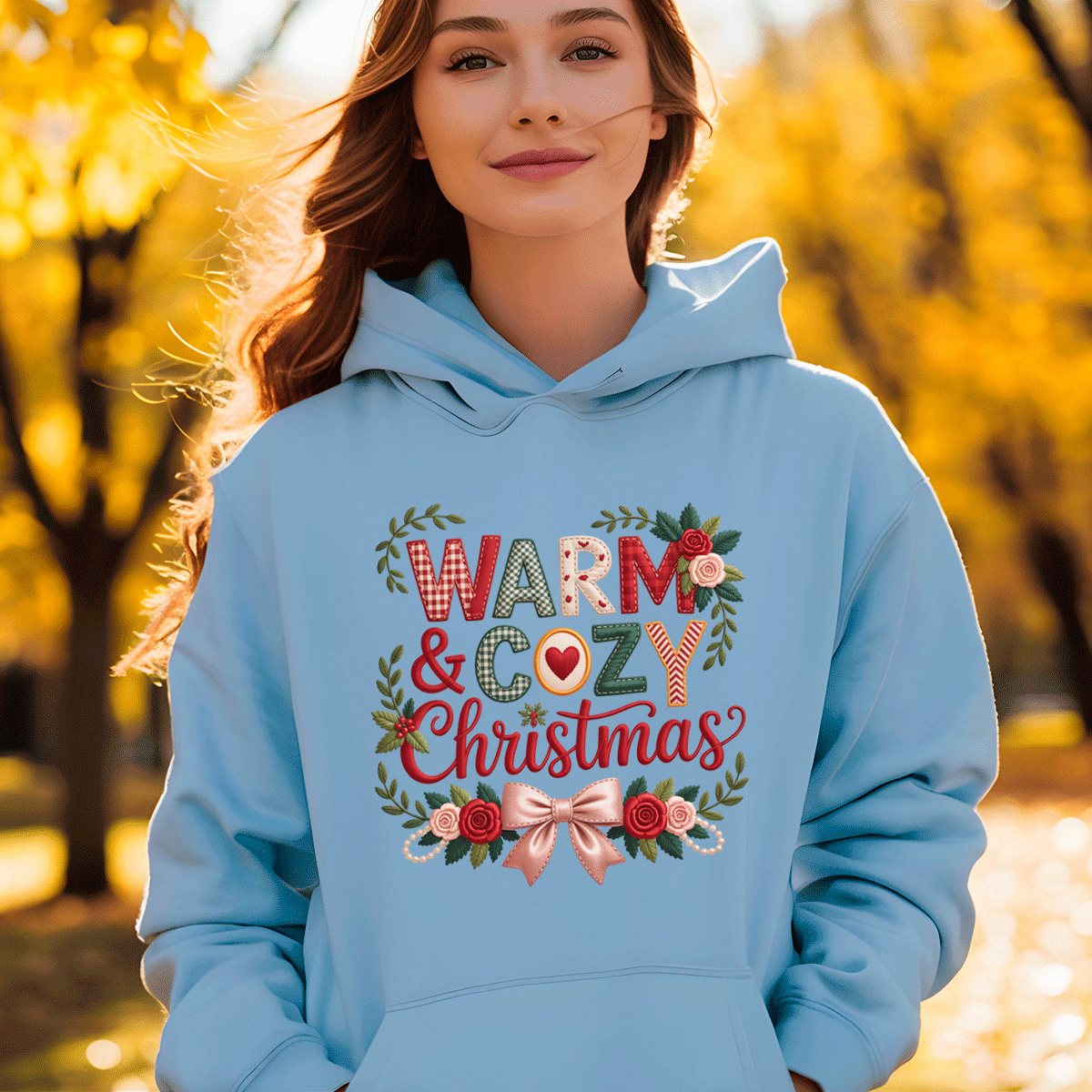 Person wearing a light blue hoodie with 'Warm & Cozy Christmas' text and decorations, standing in an autumn setting.