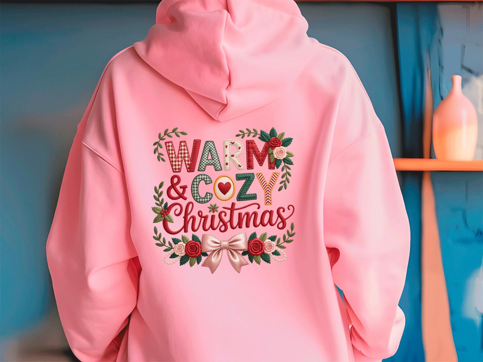 Pink hoodie with 'Warm & Cozy Christmas' text and floral design on a blue background