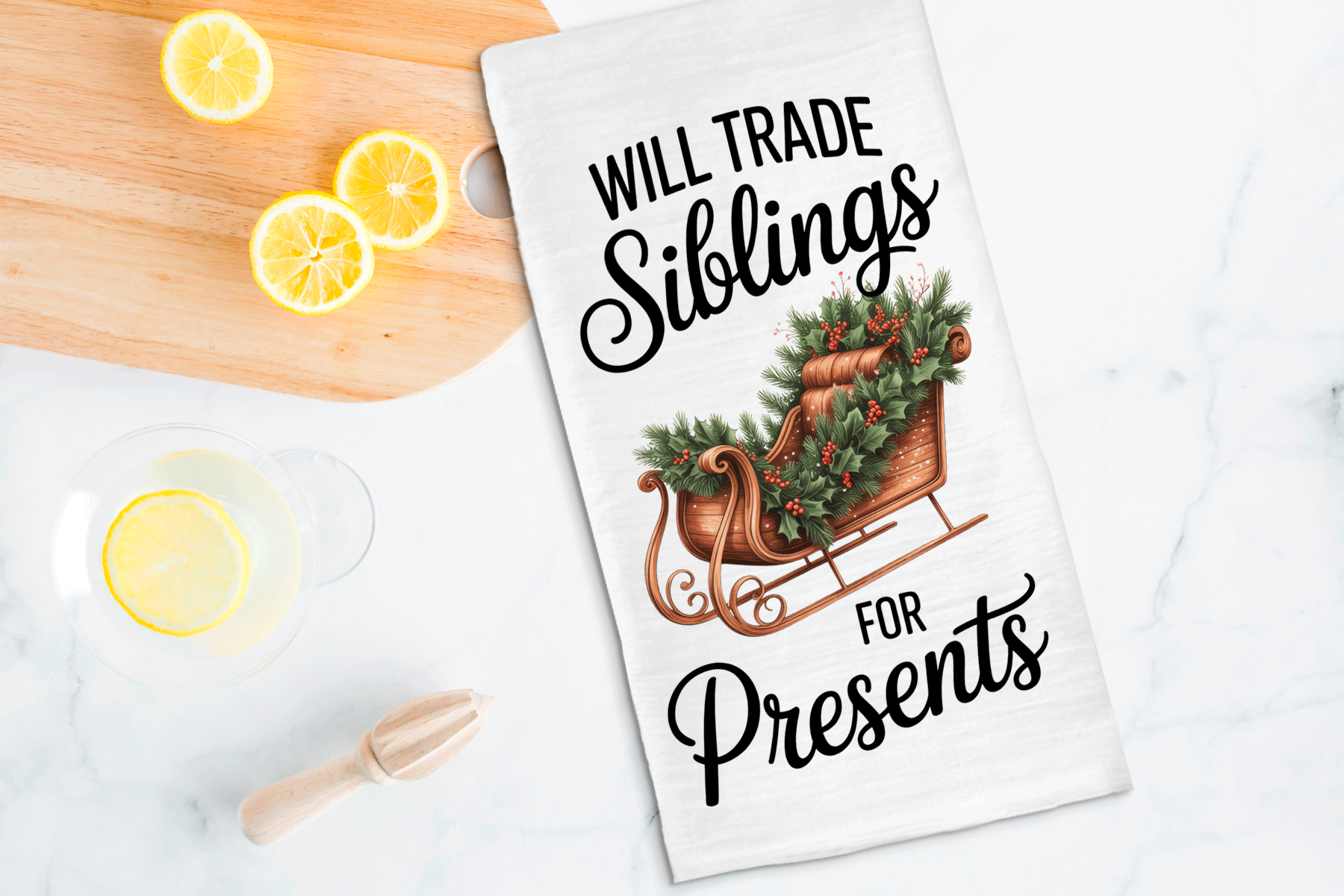 Tea towel with Christmas design and text on a kitchen counter with lemons and a wooden spoon.
