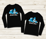 Two black long-sleeve shirts with winter-themed design on a wooden surface