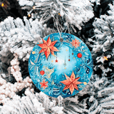 Decorative Christmas ornament with floral design hanging on a snow-covered tree.