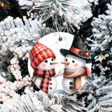 Decorative ornament with two snowmen wearing hats and scarves, hanging on a Christmas tree.