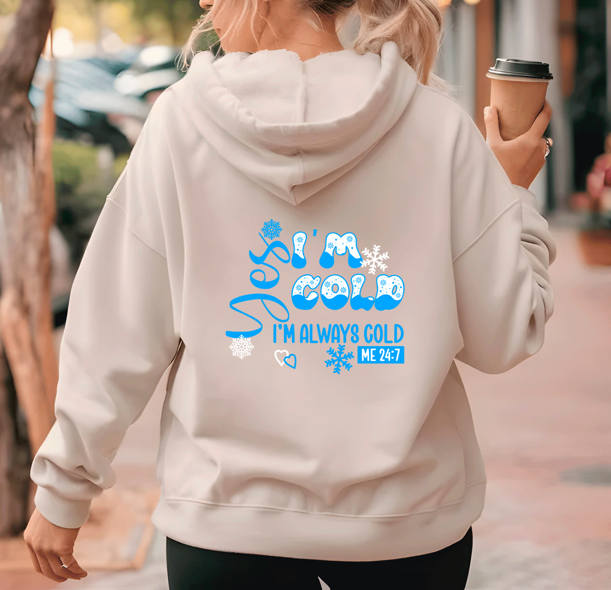 Person wearing a light gray hoodie with a humorous text design, holding a coffee cup.