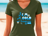 Person wearing a green V-neck t-shirt with blue text and graphics on a beach background